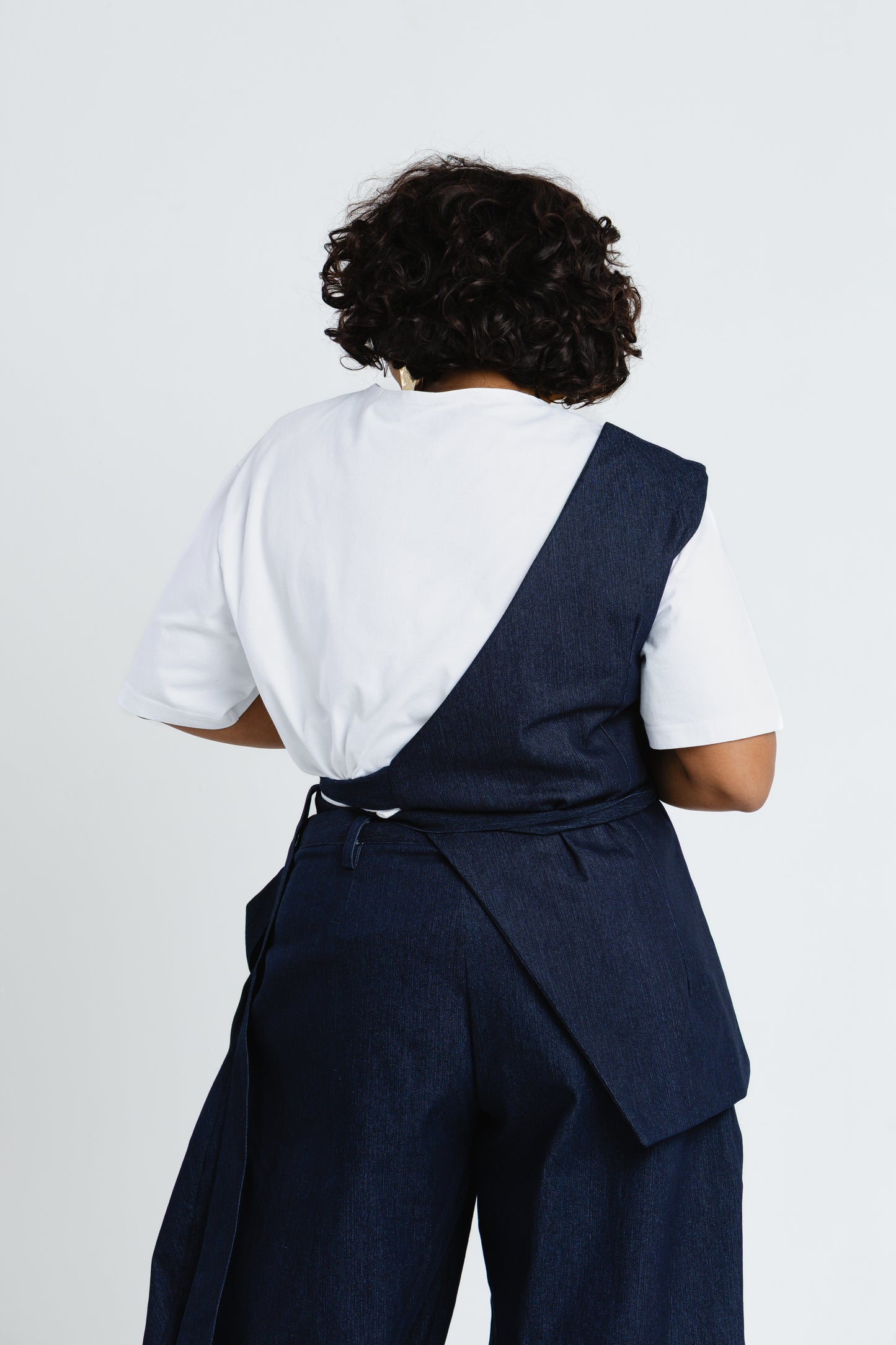 Back view of the Off Cut Denim top showing its asymmetric panel and waist tie