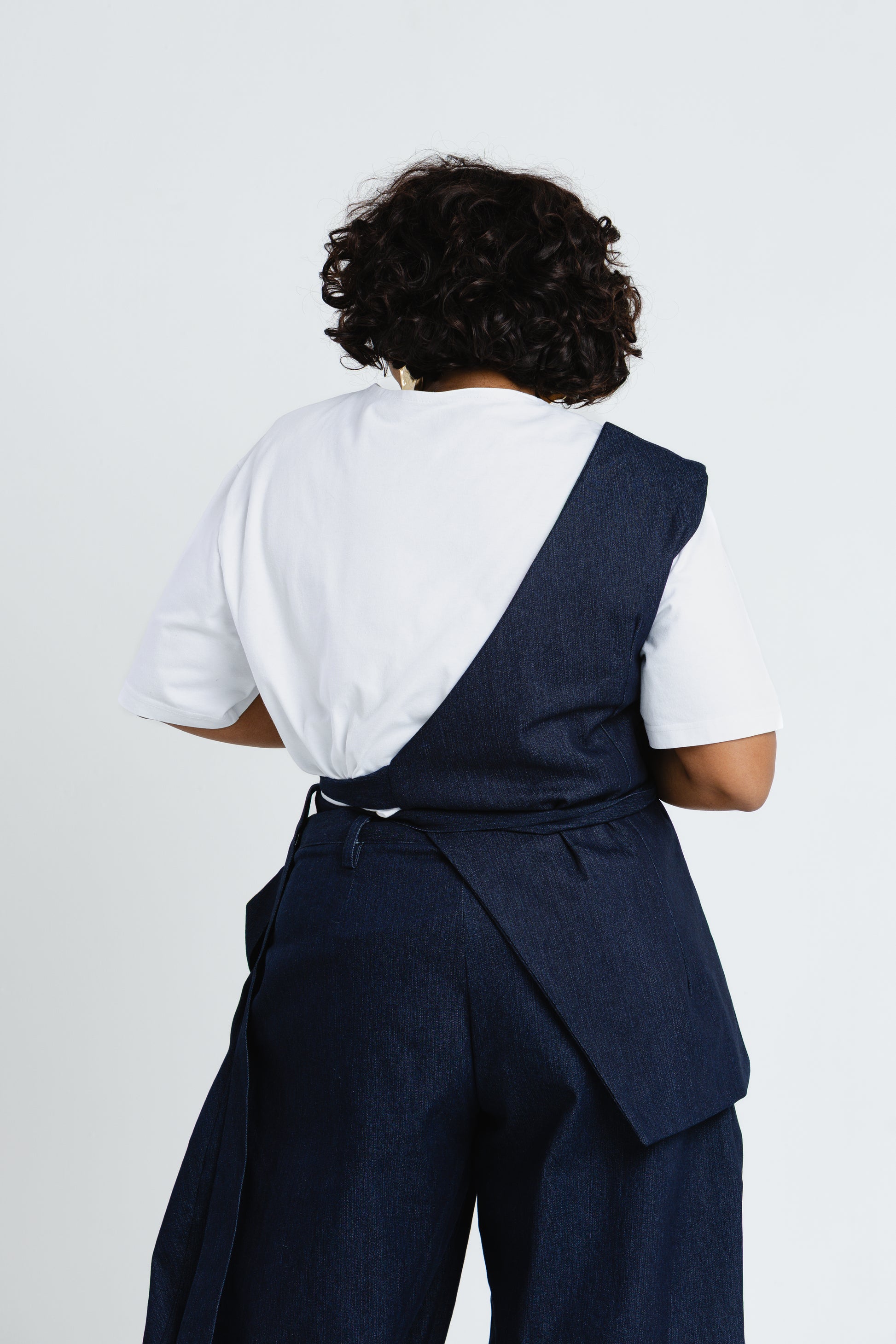 Back view of the Off Cut Denim top showing its asymmetric panel and waist tie